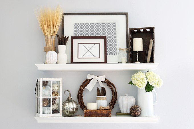 Two white wooden shelves with white flowers, and a pewter pumpkin.