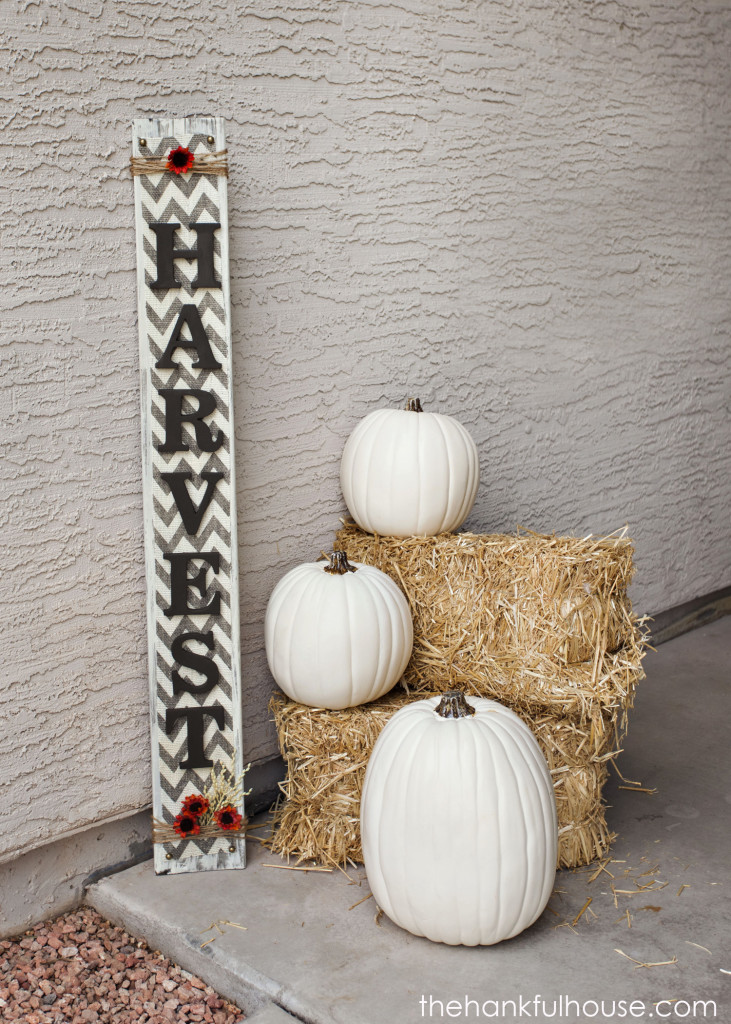 A harvest sign and 3 white pumpkins on front porch.